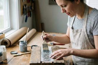 Femme appliquant un pochoir sur une caisse en bois dans un atelier DIY fait maison