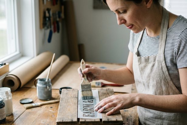 Femme appliquant un pochoir sur une caisse en bois dans un atelier DIY fait maison